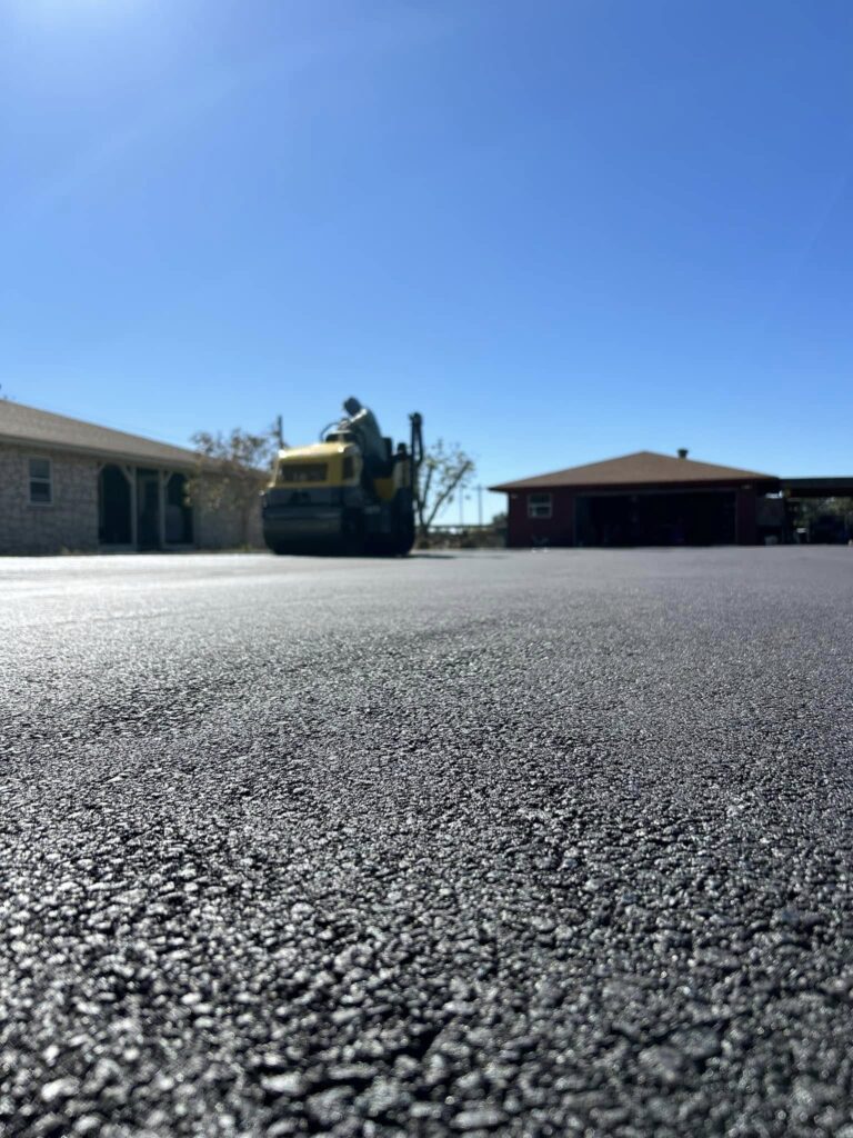 Road roller compacts asphalt outside a building