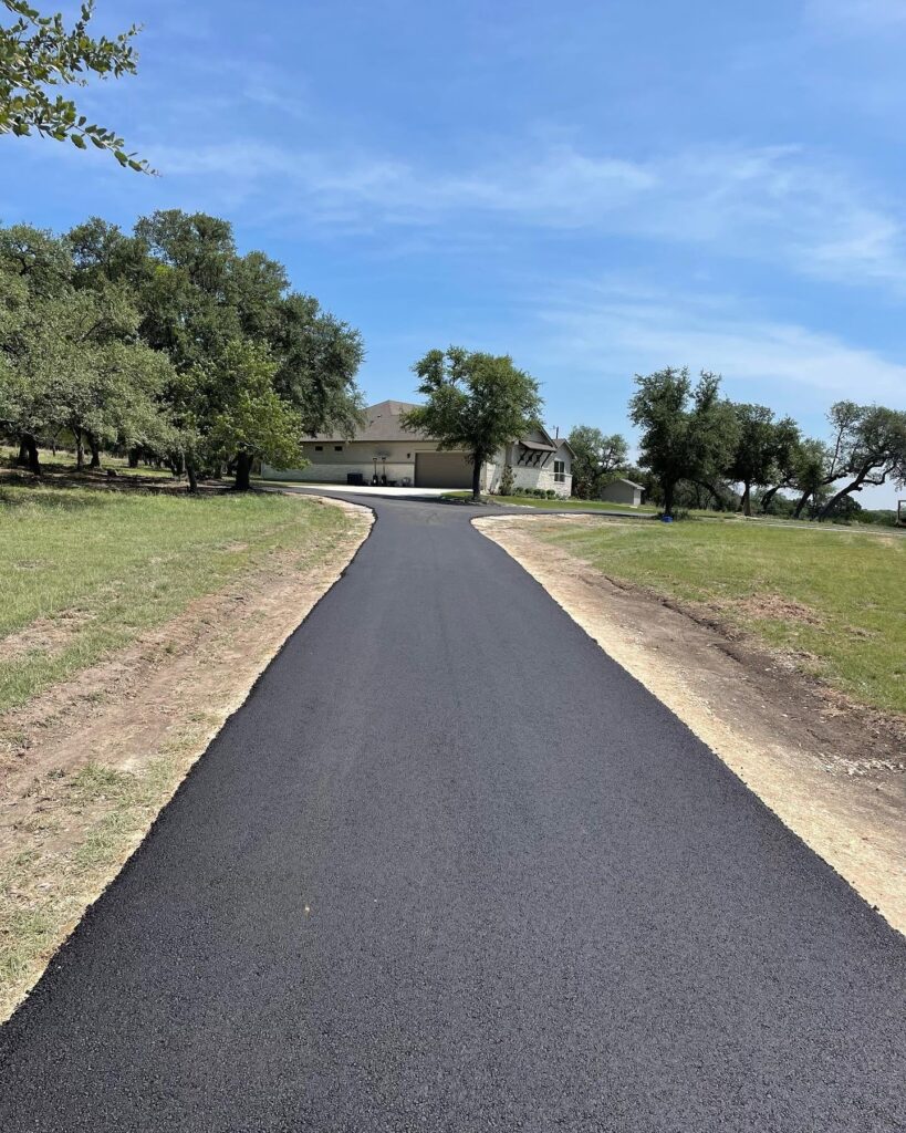 Fresh asphalt road leads toward a property entrance