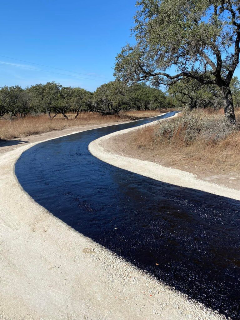Newly paved driveway curves around a dry, grassy hillside