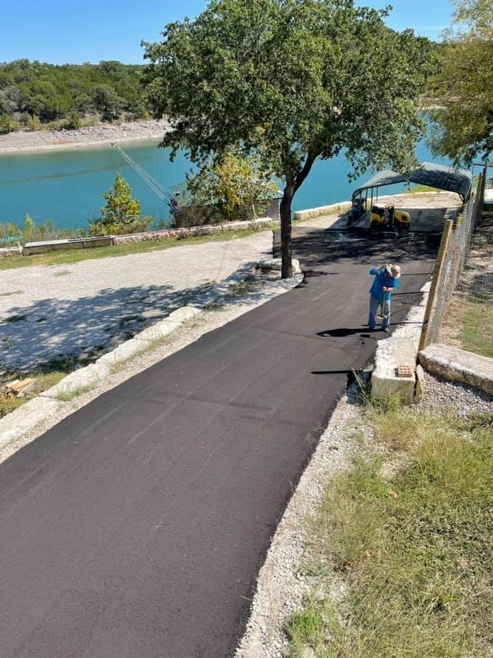 Worker stands beside a freshly paved road under trees