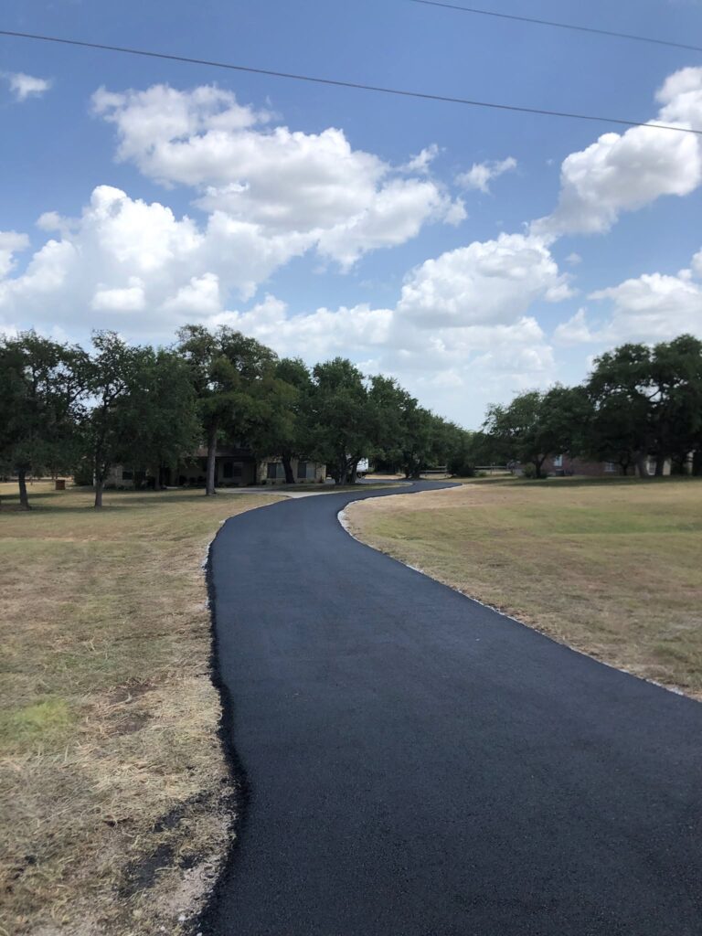 Newly paved road curves through an open, tree-lined landscape