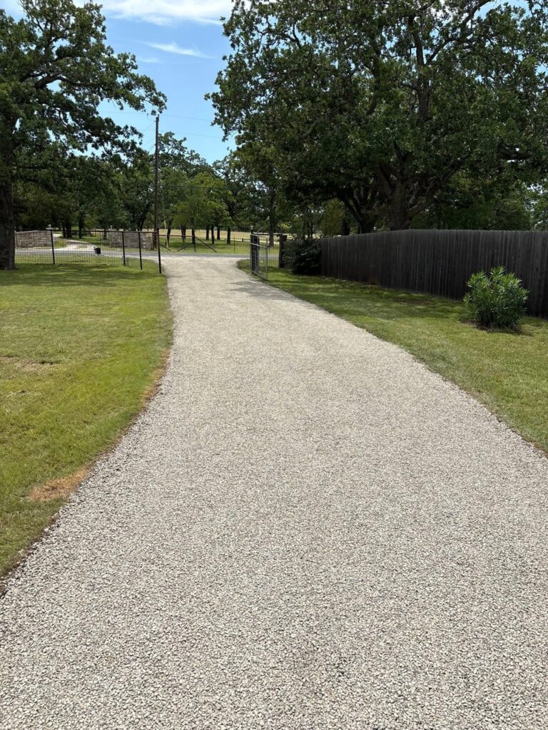 Light-colored gravel driveway leads through a fenced, tree-lined property