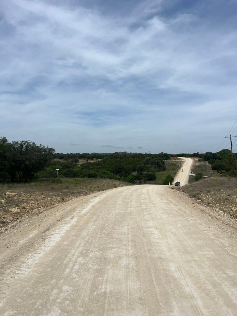 Rural road runs through open land under a cloudy sky