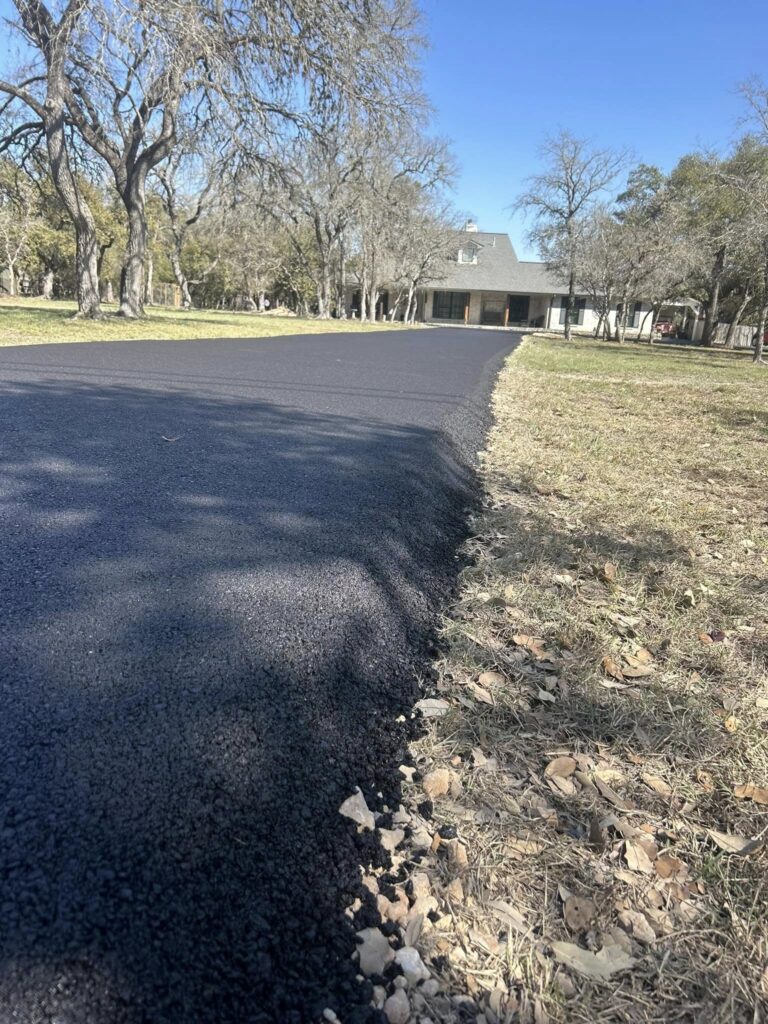 Fresh asphalt driveway curves toward a house beneath trees